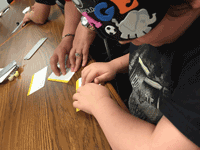 Gage reading a braille recipe at a table where others are reading and writing braille.